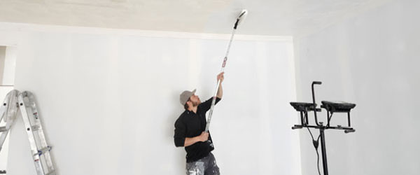 A man is painting the ceiling of a room.