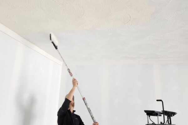 Worker in black shirt using long pole to paint ceiling
